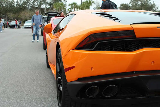 An orange Lamborghini on display at a Cars and Coffee event with crowds gathered around.